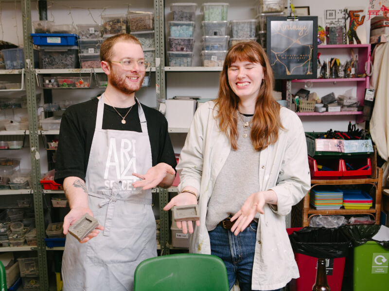 Smiling couple holding clay pieces in a workshop
